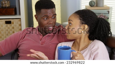 Young black woman drinking tea and chatting with boyfriend on couch
