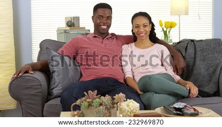 Happy young black couple relaxing on couch looking at camera