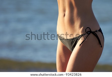 Closeup of slim woman belly in black bikini on beach