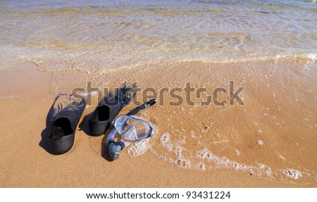 Flippers, mask and snorkel lying on sand partly in sea water, horizontal orientation