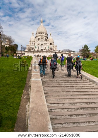 PARIS, FRANCE - APRIL 14, 2013: Tourists stroll in Montmartre near Basilica Sacre Coeur (designed by Paul Abadie, 1914) - Roman Catholic Church and minor basilica, dedicated to Sacred Heart of Jesus.