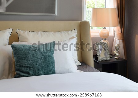 bedroom interior design with white and green pillows on white bed and decorative table lamp.