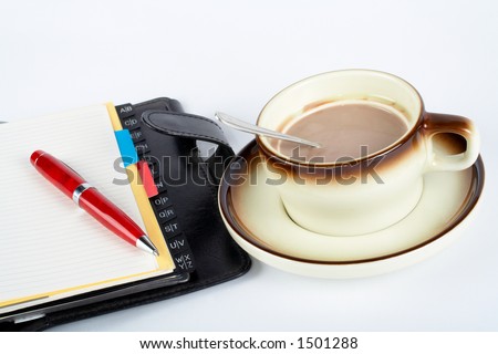 Close-up of a cup of coffee with the spoon inside and notebook with ballpoint on white background