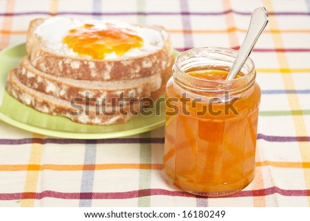 Toast with butter and peach jam glass jar in the green plate with soft shadow on square mat background. Shallow depth of field