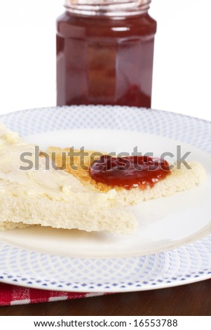 Toast with butter and strawberry jam glass jar in the white plate with soft shadow on square mat background. Shallow depth of field