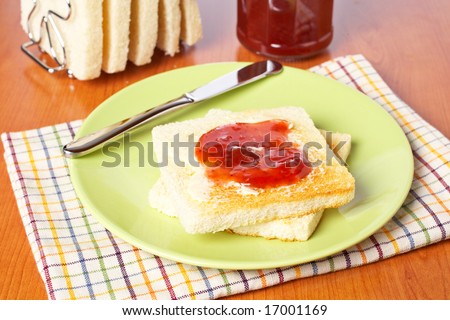 Toast with butter and strawberry jam glass jar in the white plate with soft shadow on square mat background. Shallow depth of field