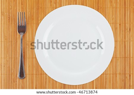 Fork and empty dinner plate with soft shadow on bamboo mat