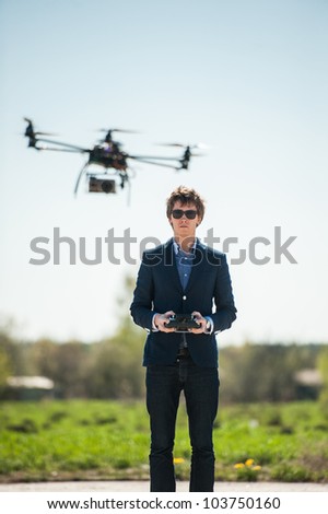 Handsome young man in suit flying remote controlled helicopter in countryside.
