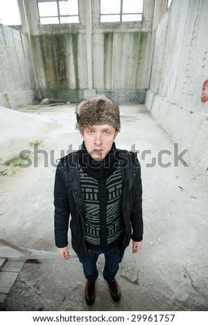 A view of a Russian man in dark clothing and hat standing in an alleyway.