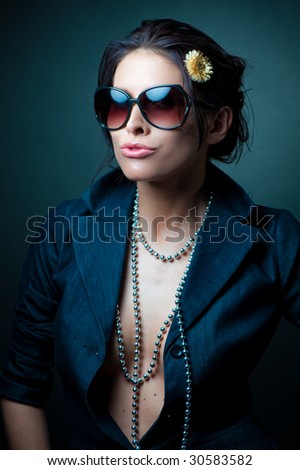Half body portrait of glamorous young woman wearing sunglasses and stylish open shirt, studio background.
