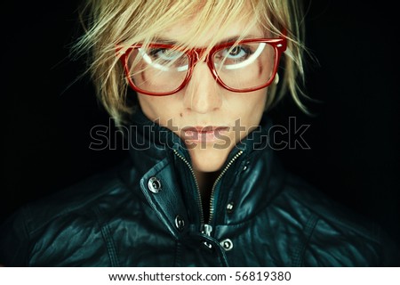 Portrait of fashionable young blond haired woman with jacket and glasses or spectacles, black background.