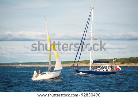 Two yachts sailing at sea by coastline with cloudscape background.