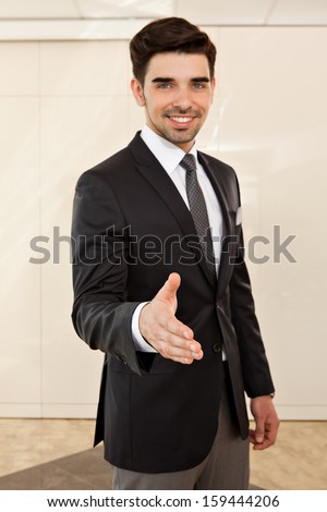 portrait of a young handsome business man smiling inviting to a handshake, focus on the hand