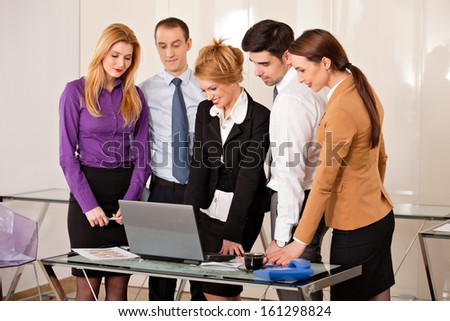Young beautiful business woman smiling with a laptop in front of her and her colleagues business people around her