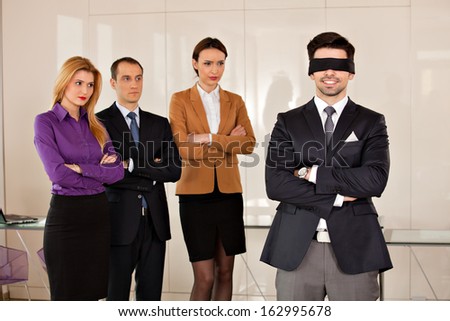concept photo of a young businessman  smiling having eyes covered, with his partners in the background, watching him with envy