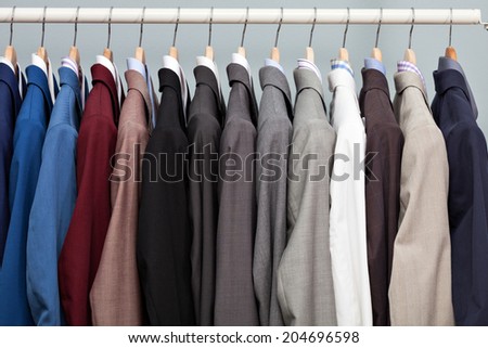 Closeup of the upper section of a row of different coloured man suits in a closet on hangers in a store or showroom