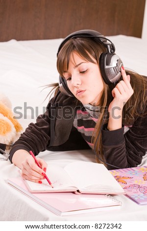 Teenage girl writing in her diary an listening to music in professional earphones
