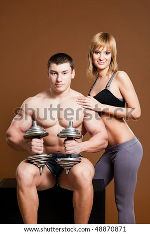 fitness couple: young man wearing short pants, holding barbells with blond fitness young woman