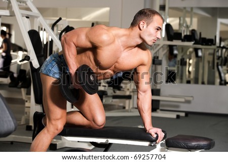 young bodybuilder training in the gym: back - dumbbell rows -finish position