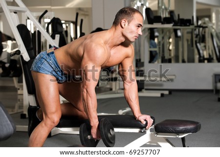 young bodybuilder training in the gym: back - dumbbell rows - start position
