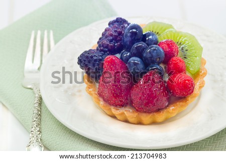 Closeup of fruit tart dessert with strawberries, blueberries, raspberries, kiwi, and blackberries with fork and napkin
