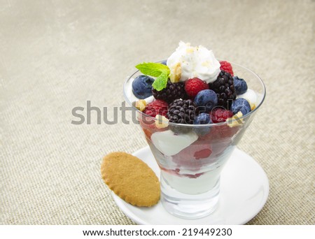 Berries with yogurt and walnuts in small dessert glass on beige textured background