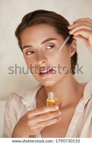 Beauty Face. Woman Applying Essential Oil On Facial Skin And Looking Away. Beautiful Model Moisturizing Derma With Natural Vitamin E, Serum Collagen And Hyaluronic Acid.