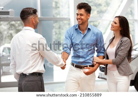 Car Showroom. Young Couple is Meeting with Seller in Auto Salon
