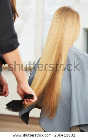 Blonde hair. Hairdresser combing long blonde hair in salon