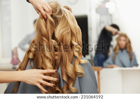 Blonde curly hair. Hairdresser doing hairstyle for young woman in salon