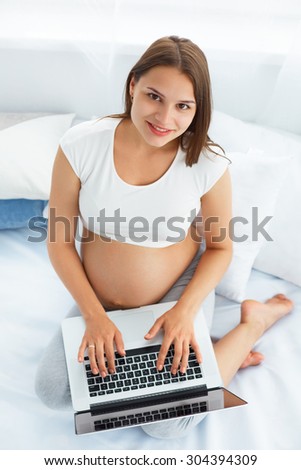 Pregnant Woman With Laptop Computer. Beautiful Pregnant Woman Working on Laptop at Home
