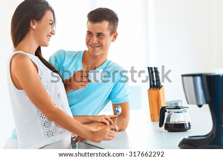Young brunette woman serving handsome man a cup of  hot black coffee. They are looking each other in the eyes and smiling.