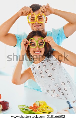 Young  couple is holding slices of bell pepper in front of their eyes smiling at the camera. Portrait of young attractive woman and handsome man having fun while cooking dinner. Vegetables are fun