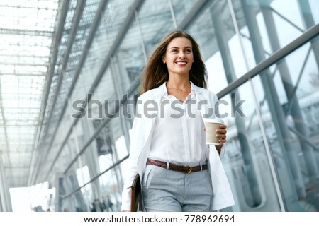 Photo of Beautiful Woman Going To Work With Coffee Walking Near Office Building. Portrait Of Successful Business Woman Holding Cup Of Hot Drink In Hand On Her Way To Work On City Street. High Resolution.