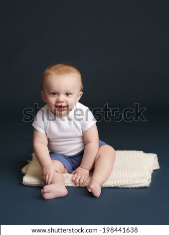 Happy baby laughing and smiling, sitting on a white blanket, dark blue studio backdrop