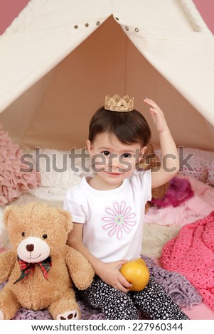 Toddler child, kid, engaged in pretend play with princess crown and teepee tent