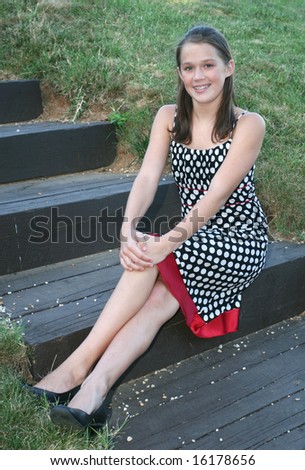 Portrait of a young girl in a dress sitting on steps in a park, outdoor setting
