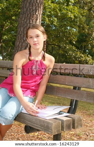 School girl writing in notebook, planner in an outdoors setting, on a bench