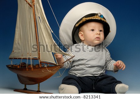Baby captain in a cap sitting next to sail boat looking up