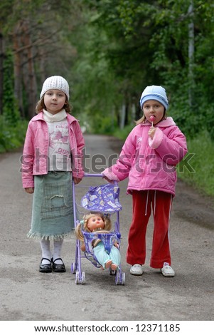 Two little girls with toy stroller and doll against green alley