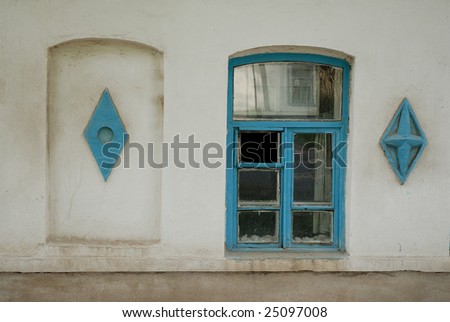 Glass window in a blue frame between two diamond shaped ornaments on plastered wall
