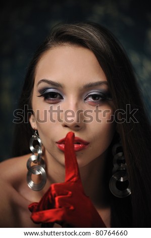 Closeup soft portrait of a glamourous young woman holding her point finger to her lips