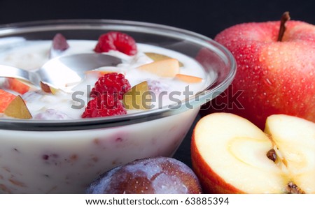 Yogurt . Glass bowl filled with yogurt mixed with fruit pieces arranged with spoon and some fruits around
