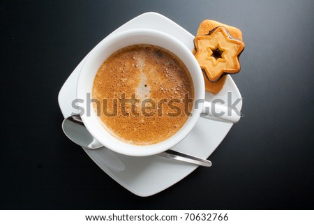 Coffee. White porcelain cup of freshly brewed coffee top view close-up arranged with two sandwich-biscuits, spoon and plate on dark background