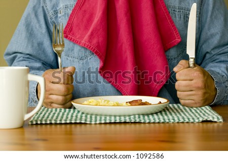 Ready For Breakfast Hungry man holding knife and fork with napkin tucked in shirt ready to eat bacon and eggs for breakfast.