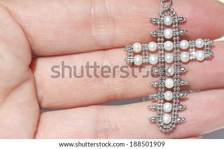 White gold pendant in the shape of a crucifix with beads in the hand of a woman on a white background