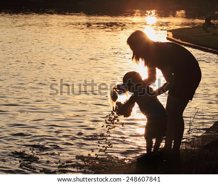 the silhouette family(mother and son)feeding fish in the park