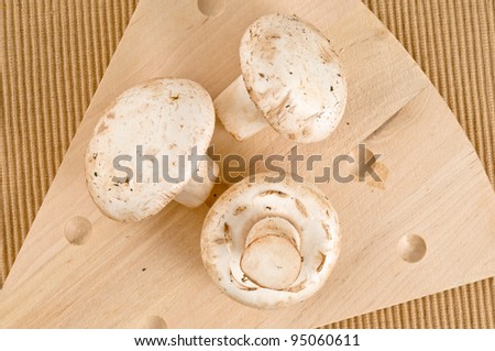 A wood cutting board with three white mushrooms top view