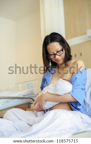 Beautiful new mother happy holding her infant baby and feeding her milk to her baby after giving birth in hospital.