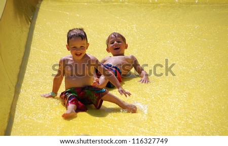 Riding the Slide/Two boys slide down the 	water slide in the sun
